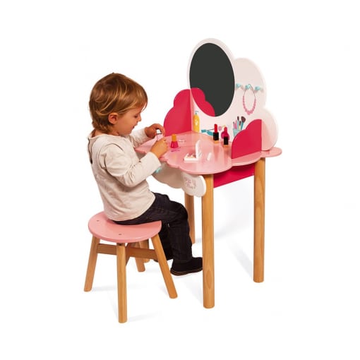 Little girl sits in front of wooden table with mirror on wooden stool.